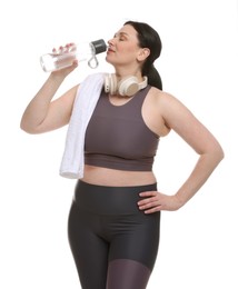 Plus size woman in gym clothes drinking water on white background