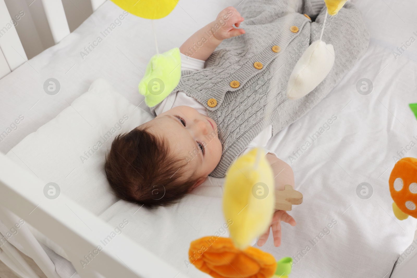 Photo of Cute little baby in crib with cot mobile at home