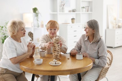 Friendship. Senior women building tower with wooden blocks at wooden table indoors