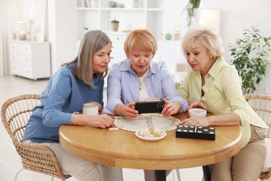 Photo of Friendship. Senior women watching something on smartphone at table indoors