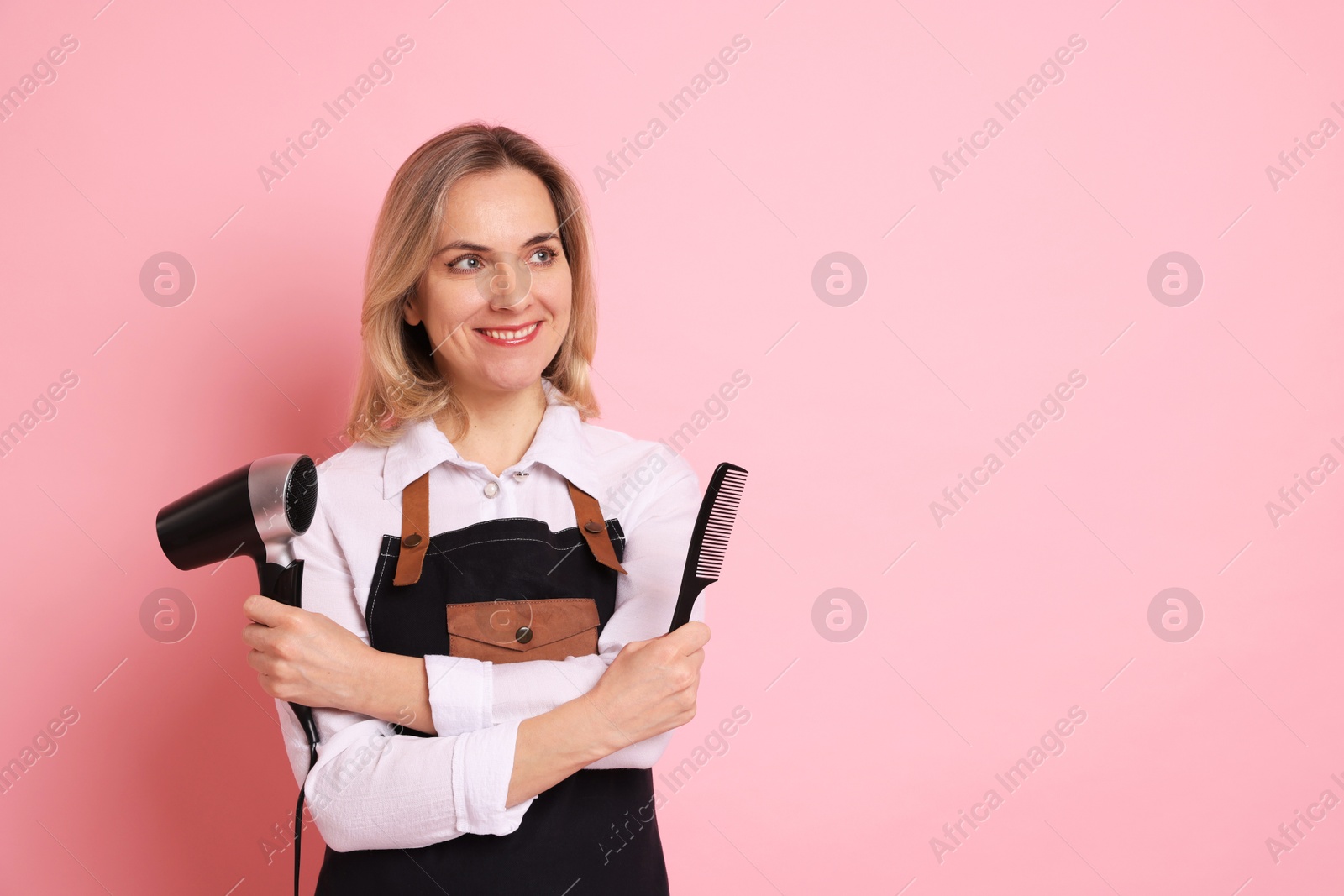 Photo of Smiling hairdresser with dryer and comb on pink background, space for text