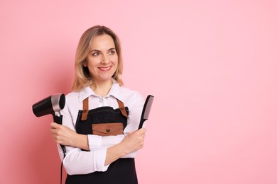 Smiling hairdresser with dryer and comb on pink background, space for text