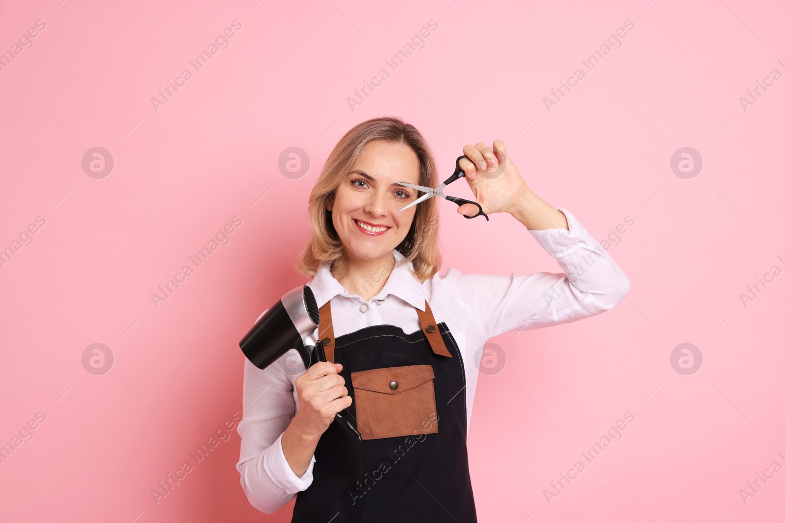 Photo of Smiling hairdresser with dryer and scissors on pink background