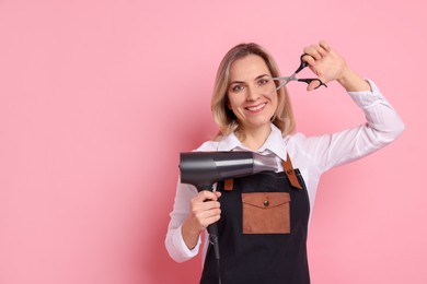 Smiling hairdresser with dryer and scissors on pink background, space for text