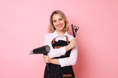 Photo of Smiling hairdresser with dryer, scissors and comb on pink background