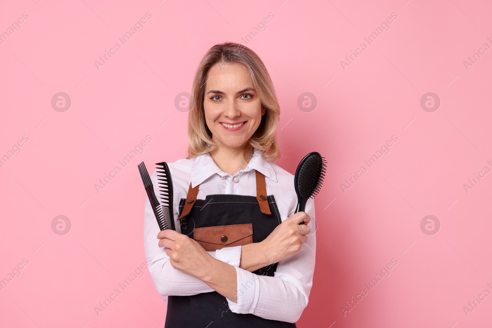 Photo of Smiling hairdresser with combs and brush on pink background