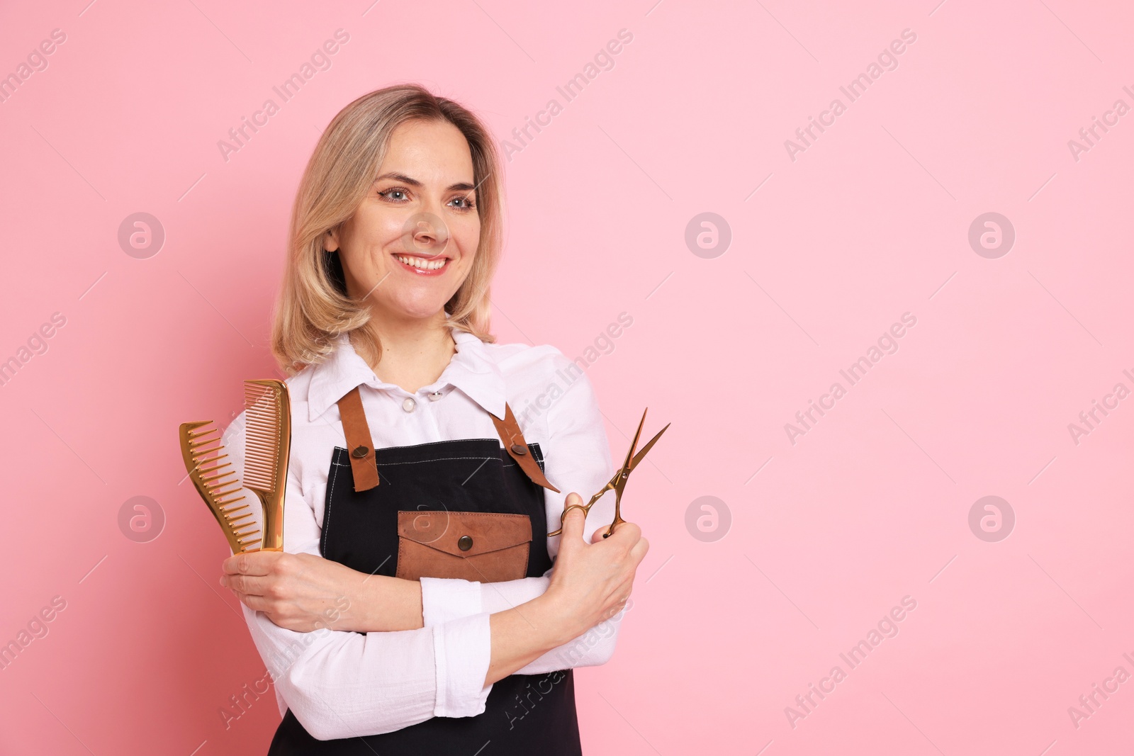 Photo of Smiling hairdresser with combs and scissors on pink background, space for text