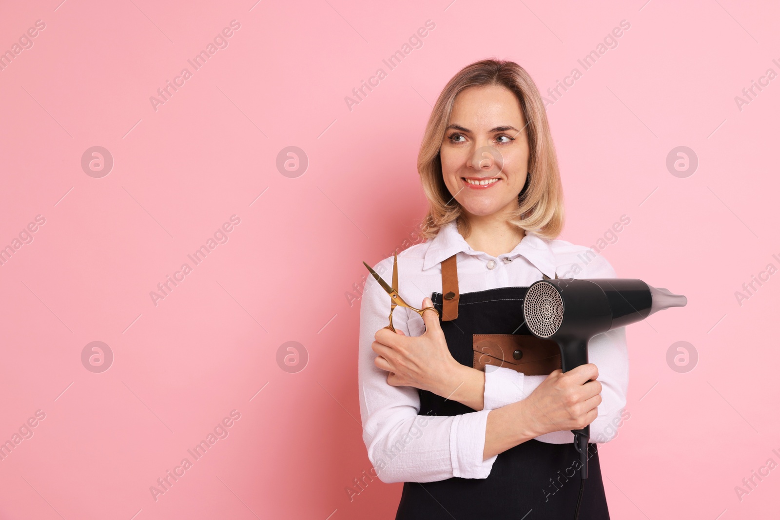 Photo of Smiling hairdresser with dryer and scissors on pink background, space for text