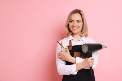 Smiling hairdresser with dryer and scissors on pink background, space for text