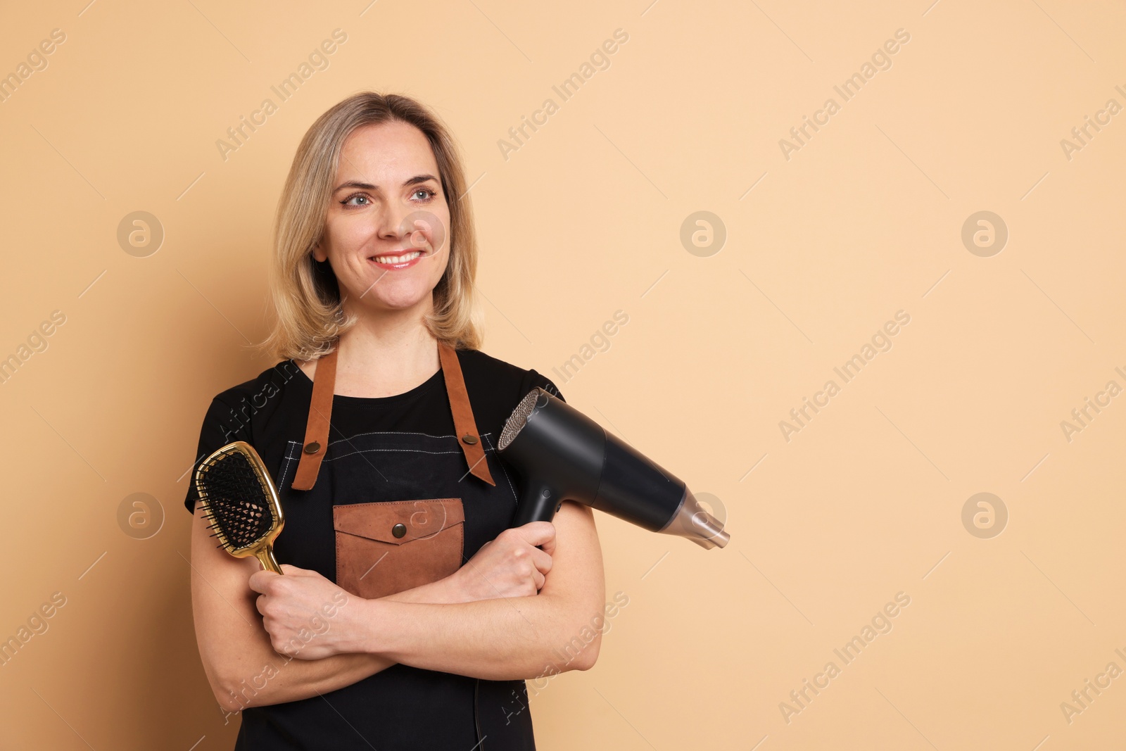 Photo of Smiling hairdresser with dryer and brush on beige background, space for text