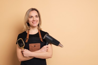 Smiling hairdresser with dryer and brush on beige background, space for text