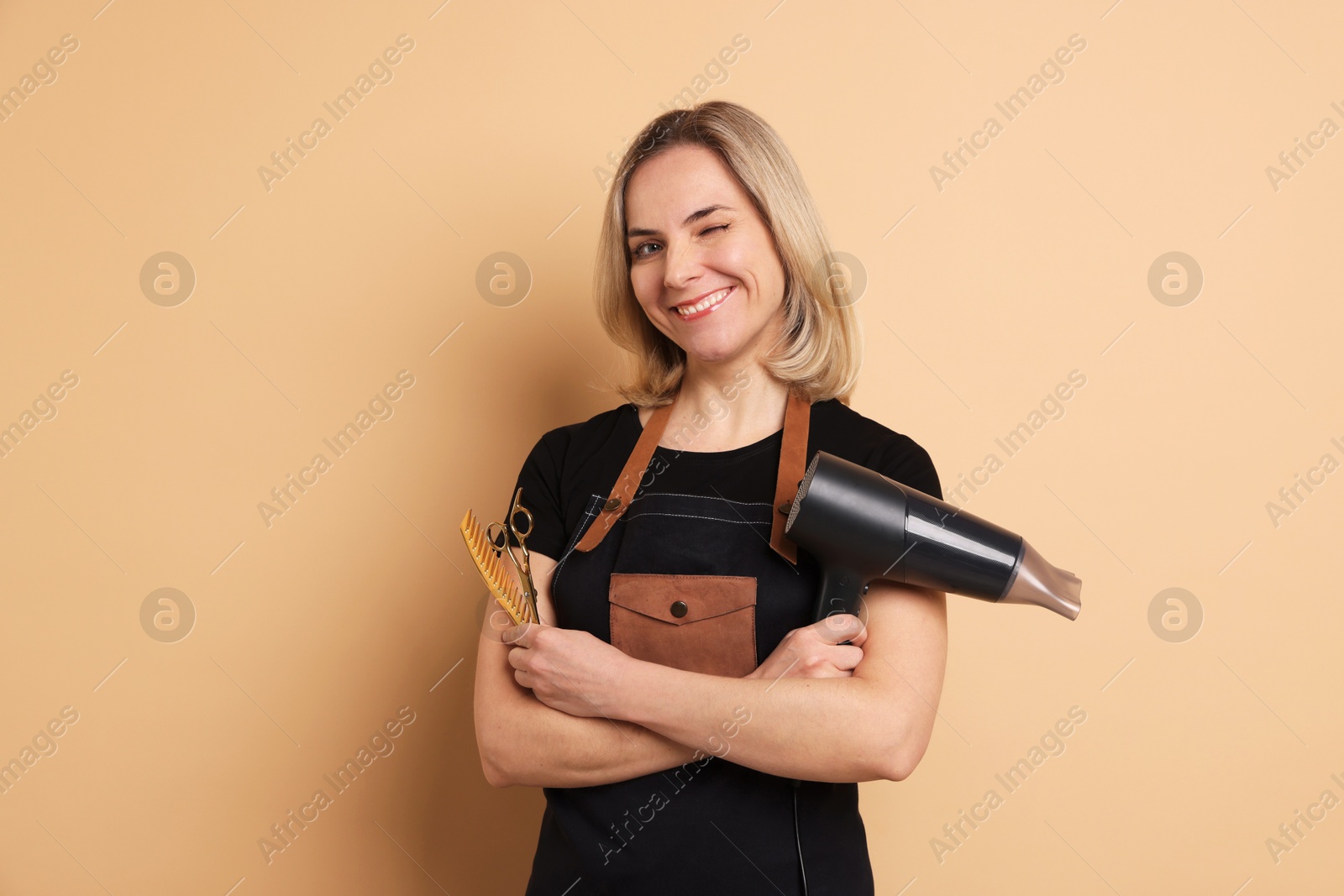 Photo of Smiling hairdresser with dryer, scissors and comb on beige background