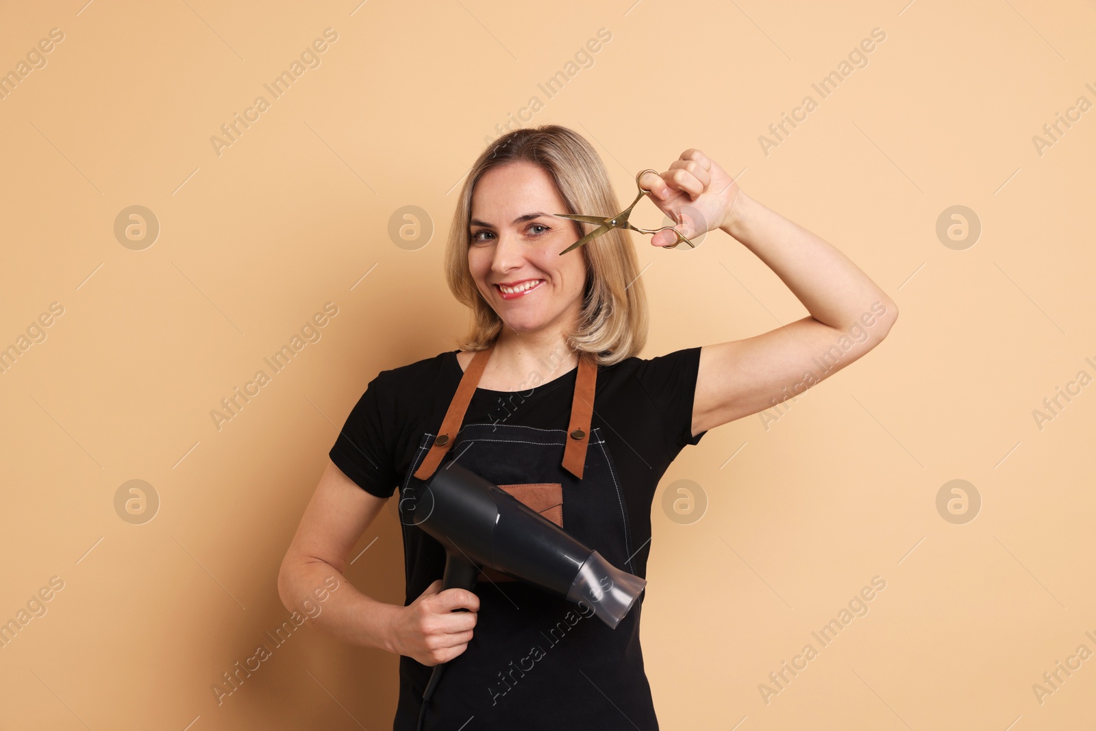 Photo of Smiling hairdresser with dryer and scissors on beige background