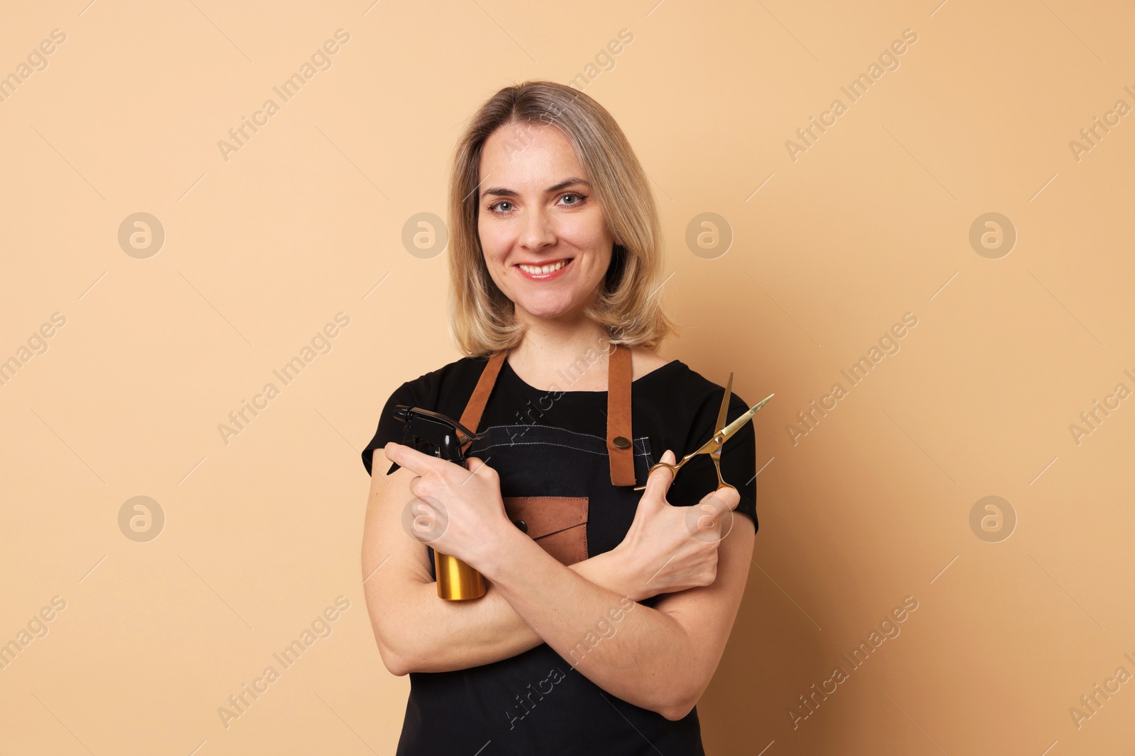 Photo of Smiling hairdresser with scissors and spray bottle on beige background