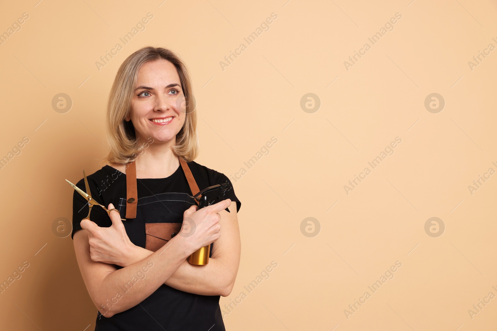 Photo of Smiling hairdresser with scissors and spray bottle on beige background, space for text