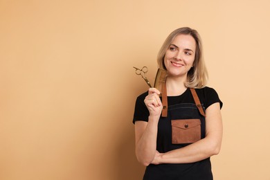 Photo of Smiling hairdresser with scissors and comb on beige background, space for text