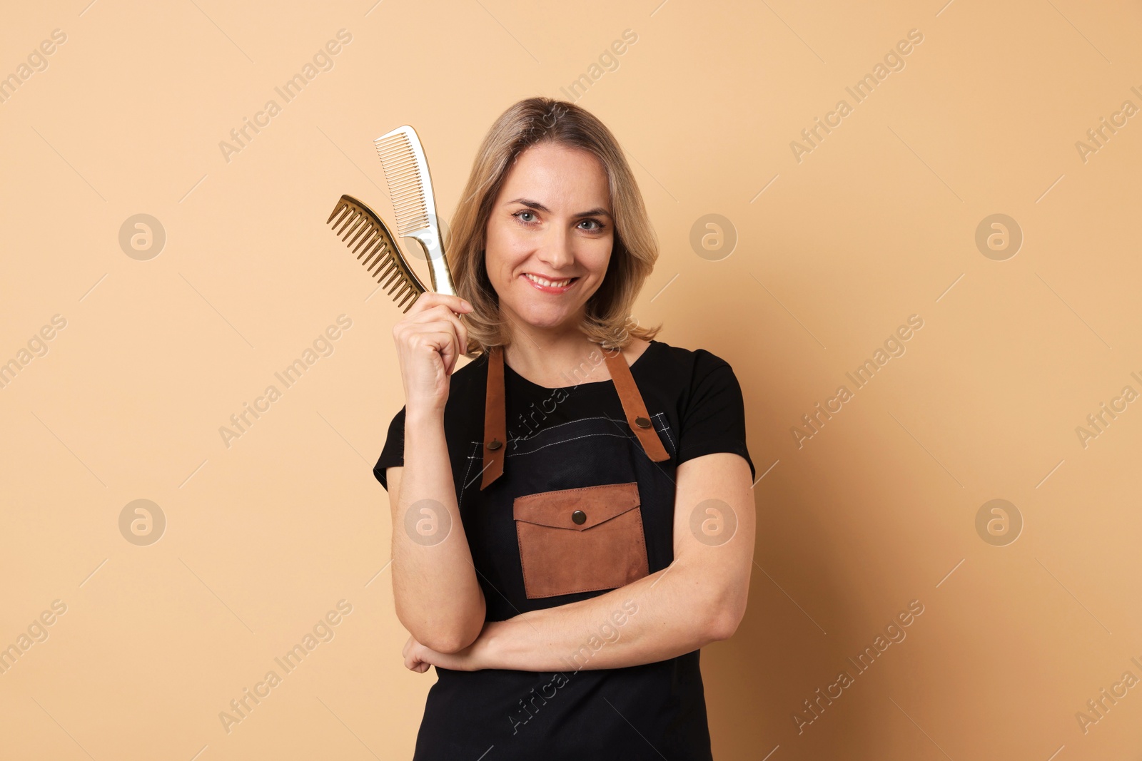 Photo of Smiling hairdresser with combs on beige background