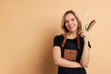 Photo of Smiling hairdresser with combs on beige background, space for text