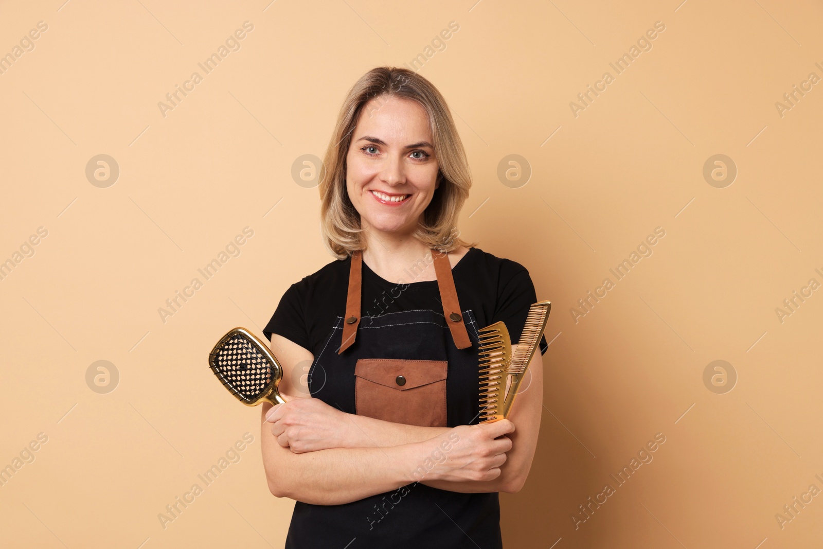 Photo of Smiling hairdresser with brush and combs on beige background