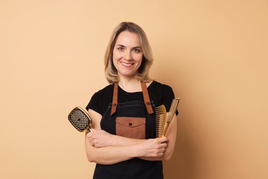 Smiling hairdresser with brush and combs on beige background