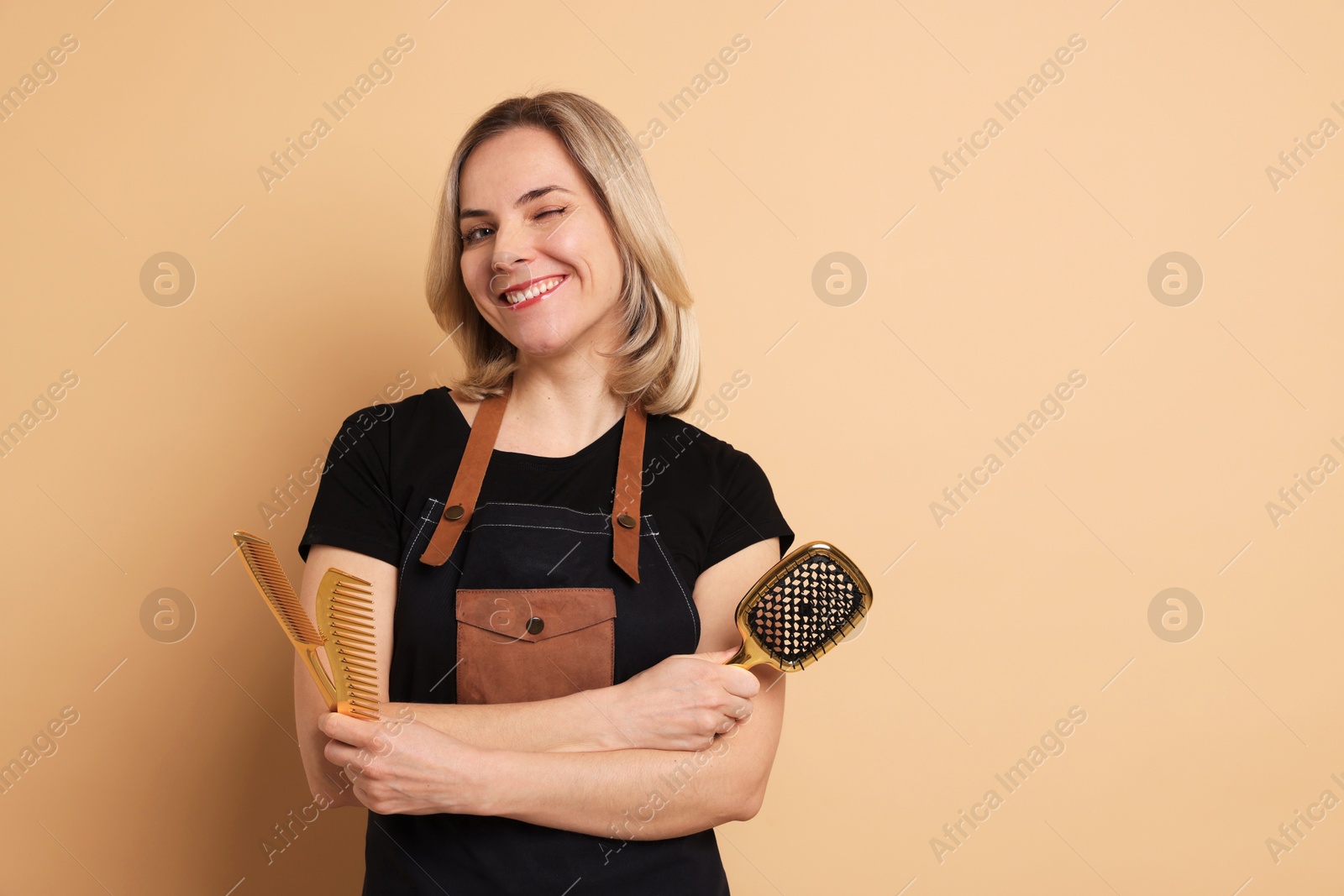 Photo of Smiling hairdresser with brush and combs on beige background, space for text