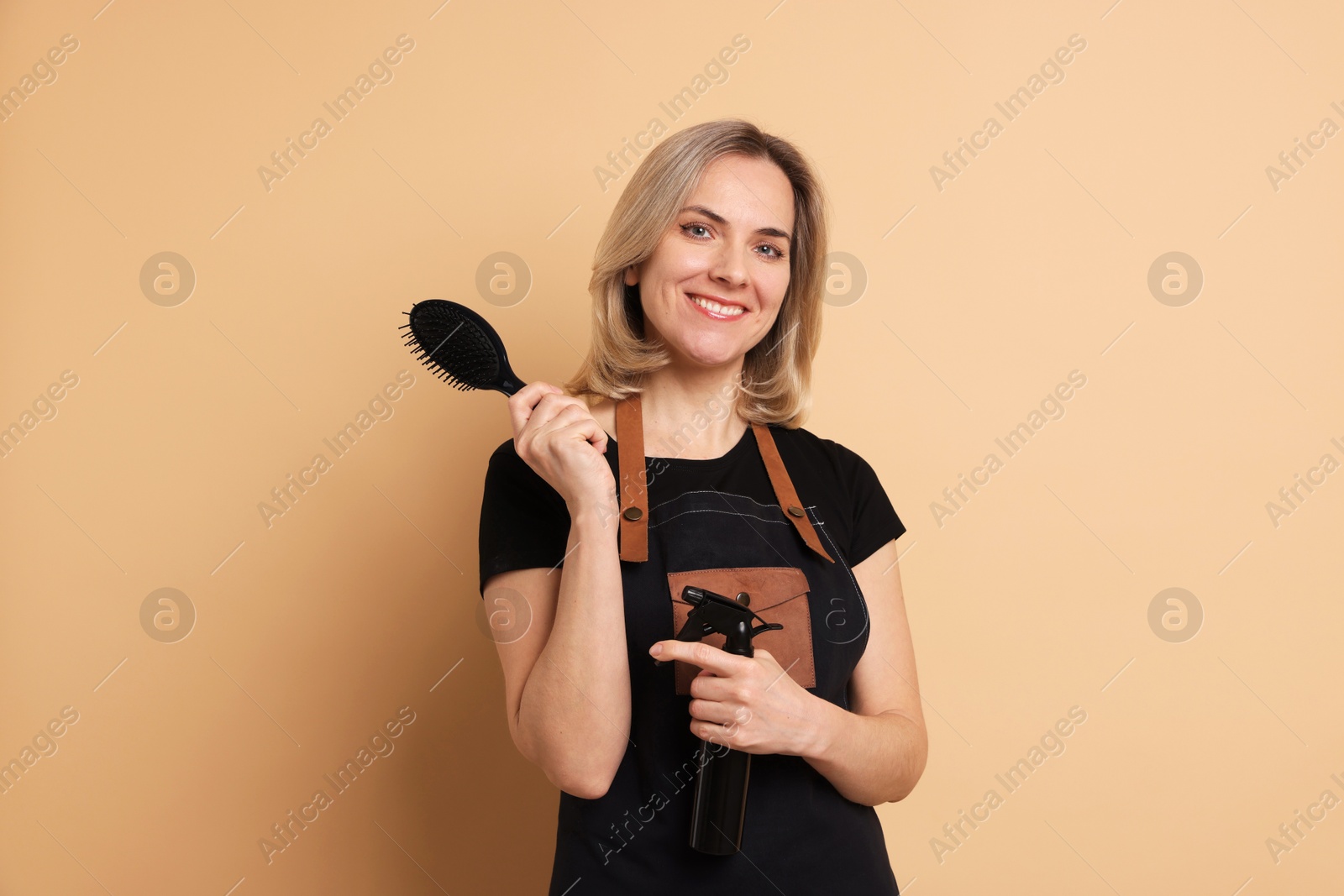 Photo of Smiling hairdresser with brush and spray bottle on beige background