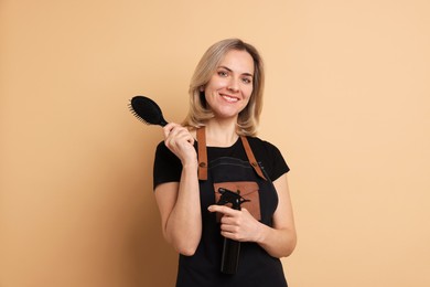 Photo of Smiling hairdresser with brush and spray bottle on beige background