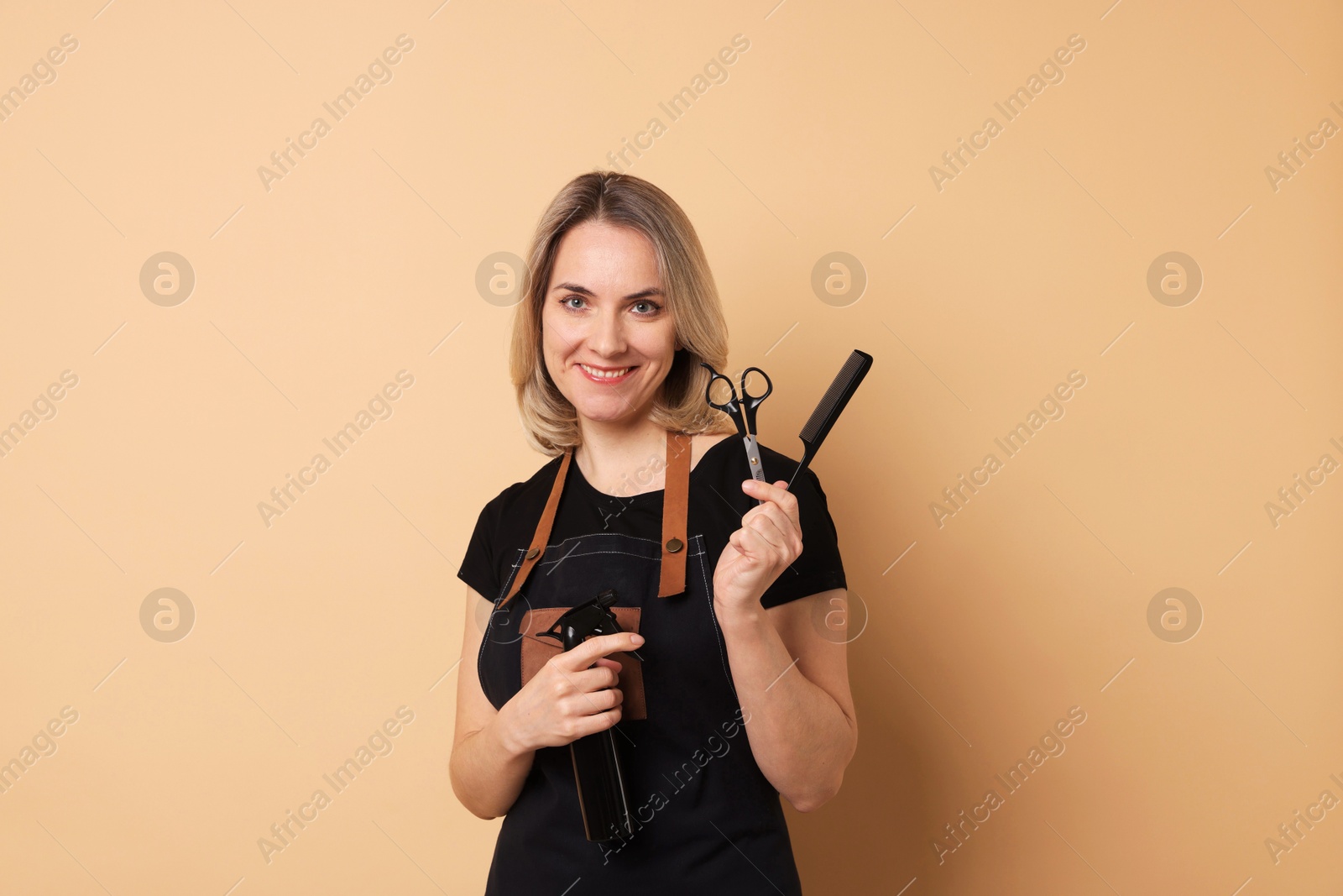 Photo of Smiling hairdresser with comb, scissors and spray bottle on beige background