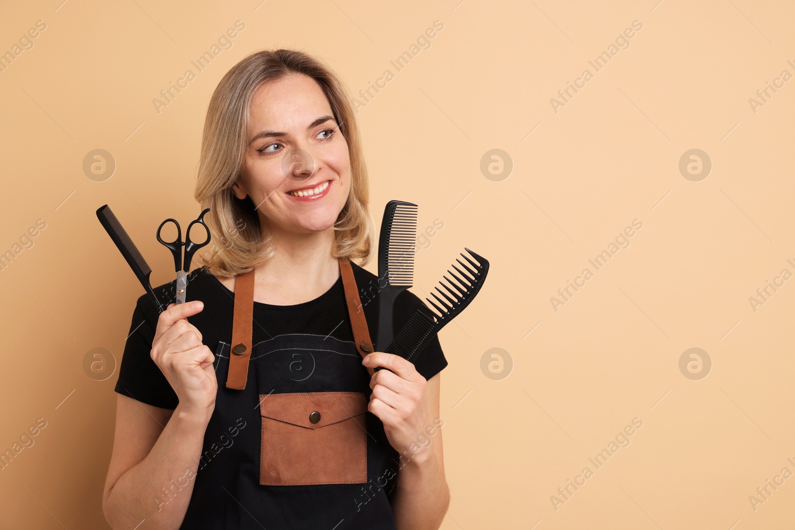 Photo of Smiling hairdresser with combs and scissors on beige background, space for text