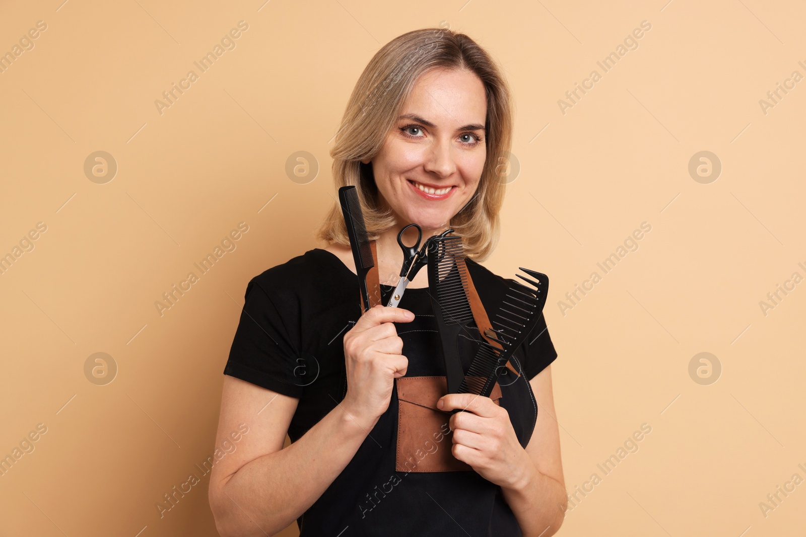 Photo of Smiling hairdresser with combs and scissors on beige background