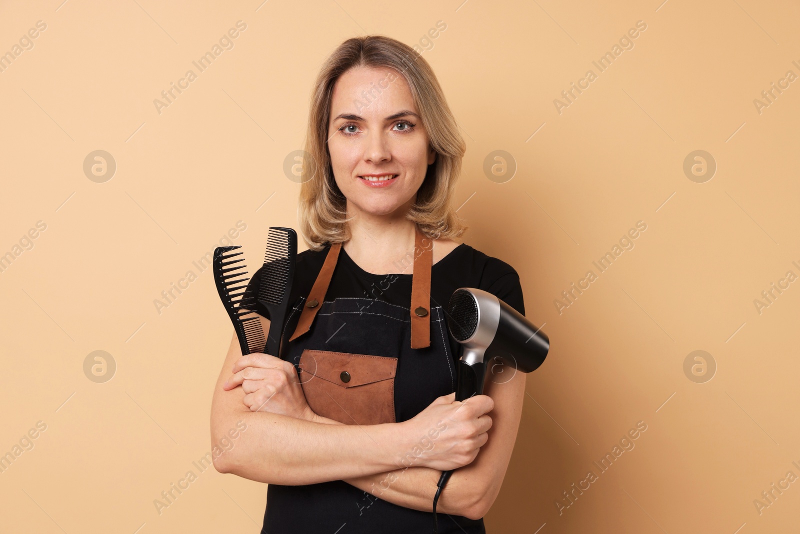 Photo of Smiling hairdresser with combs and dryer on beige background