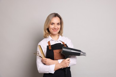 Photo of Smiling hairdresser with dryer, scissors and comb on gray background