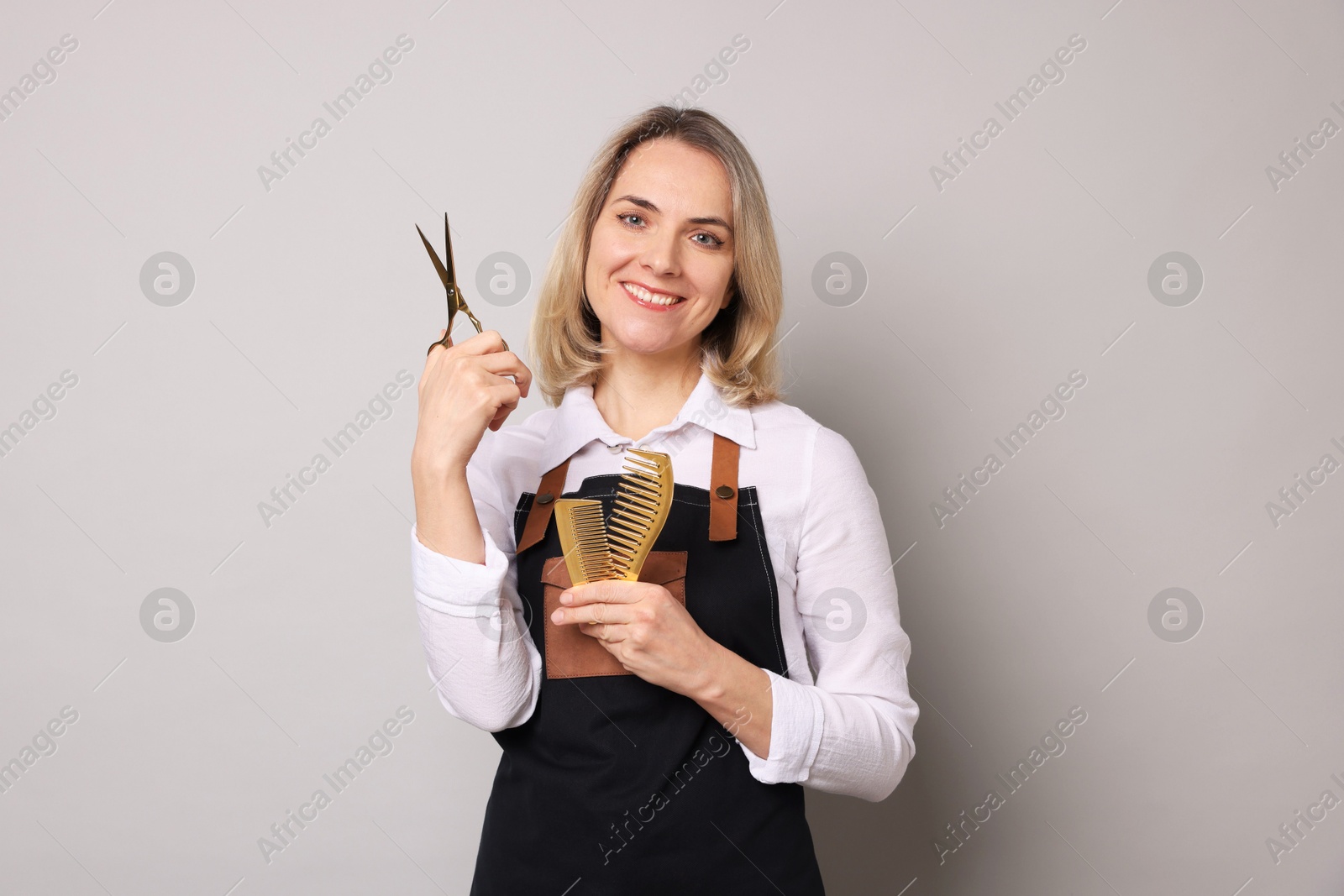 Photo of Smiling hairdresser with scissors and combs on gray background