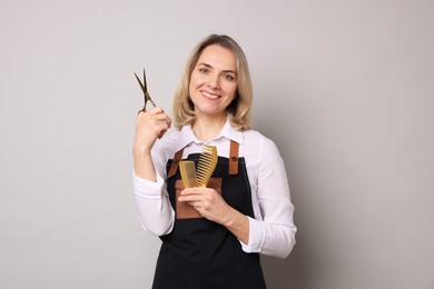 Photo of Smiling hairdresser with scissors and combs on gray background