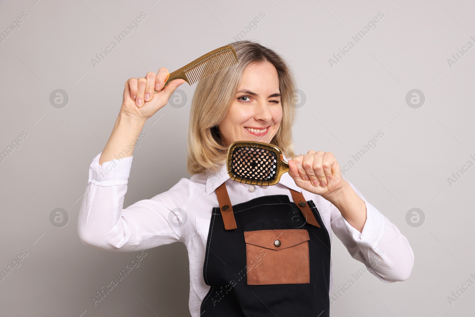 Photo of Smiling hairdresser with brush and comb on gray background