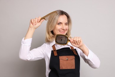 Smiling hairdresser with brush and comb on gray background