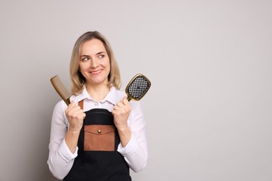 Photo of Smiling hairdresser with brush and comb on gray background, space for text