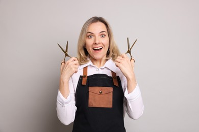 Surprised hairdresser with scissors on gray background