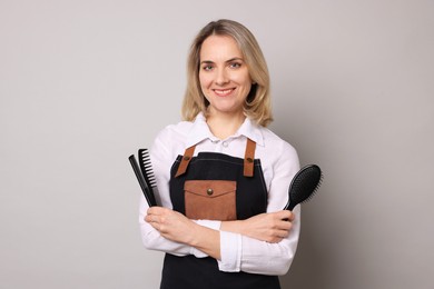 Smiling hairdresser with combs and brush on gray background