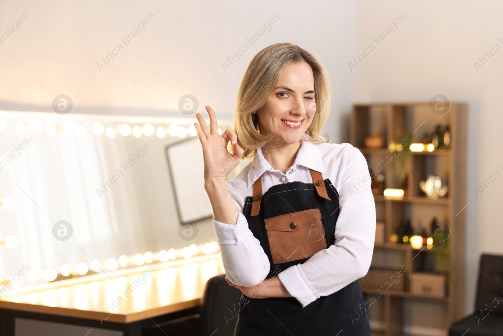 Photo of Smiling hairdresser showing OK gesture in beauty salon