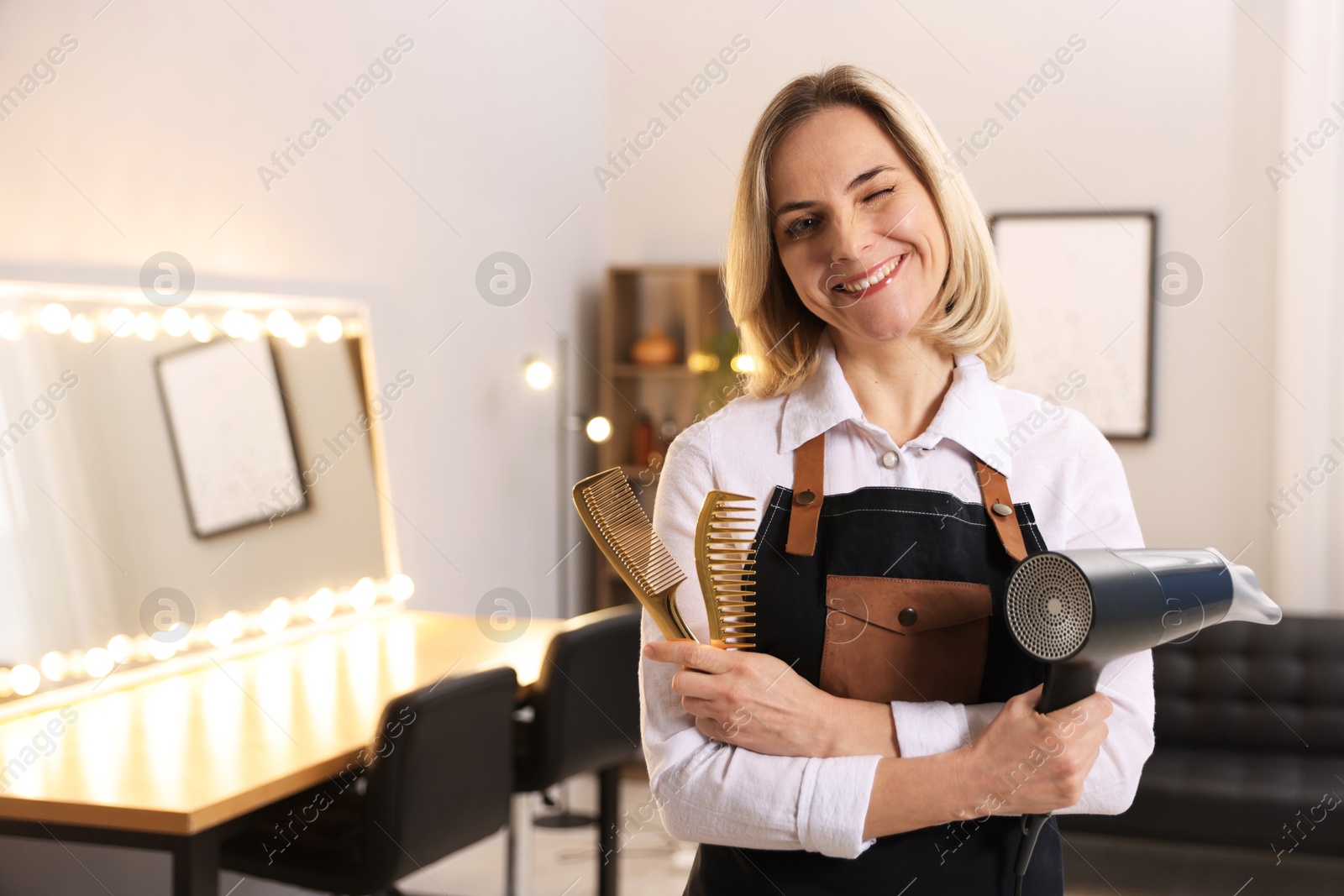 Photo of Smiling hairdresser with dryer and combs in beauty salon, space for text