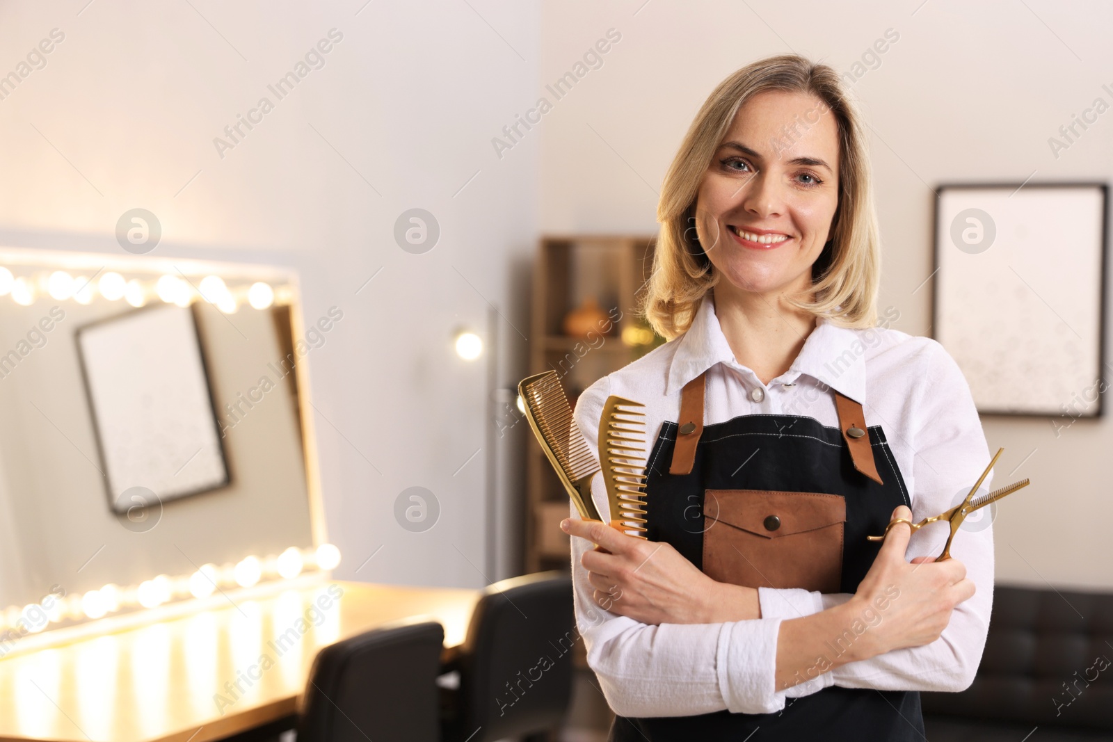 Photo of Smiling hairdresser with combs and scissors in beauty salon, space for text