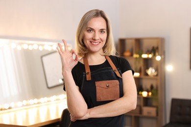 Smiling hairdresser showing OK gesture in beauty salon