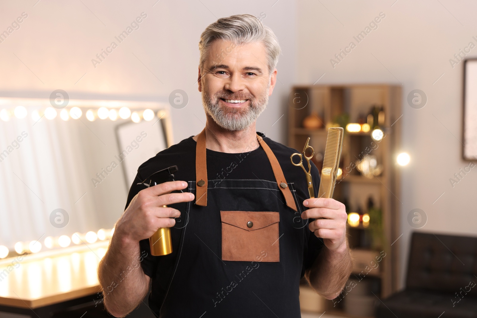 Photo of Smiling hairdresser with spray bottle, comb and scissors in beauty salon