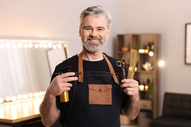 Smiling hairdresser with spray bottle, comb and scissors in beauty salon