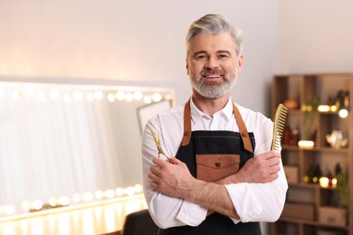 Smiling hairdresser with scissors and comb in beauty salon, space for text