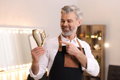 Photo of Smiling hairdresser with scissors and comb in beauty salon