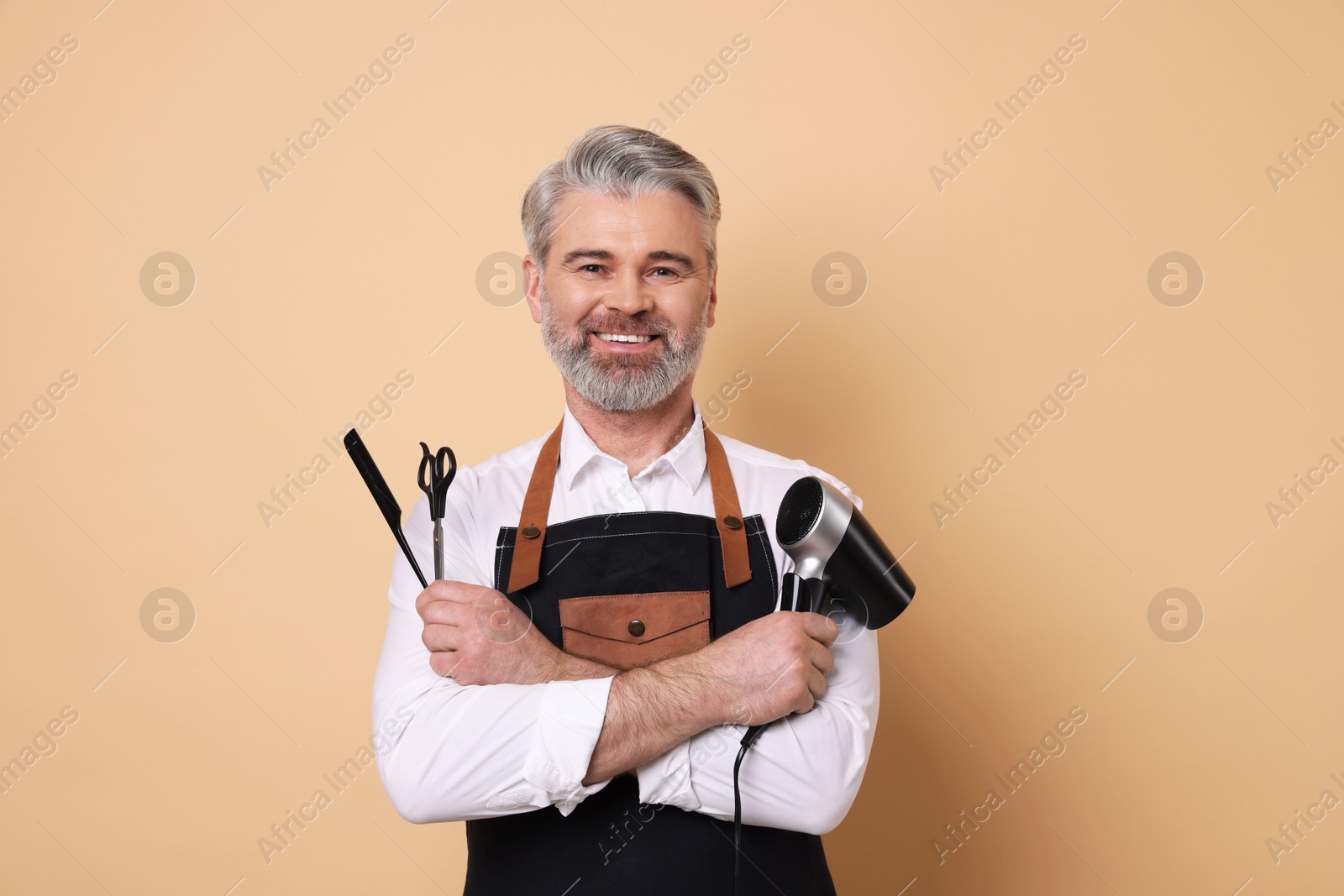 Photo of Smiling hairdresser with dryer, scissors and comb on beige background