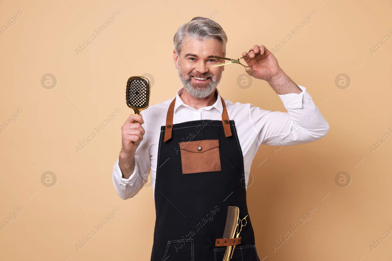 Photo of Smiling hairdresser with scissors and brush on beige background