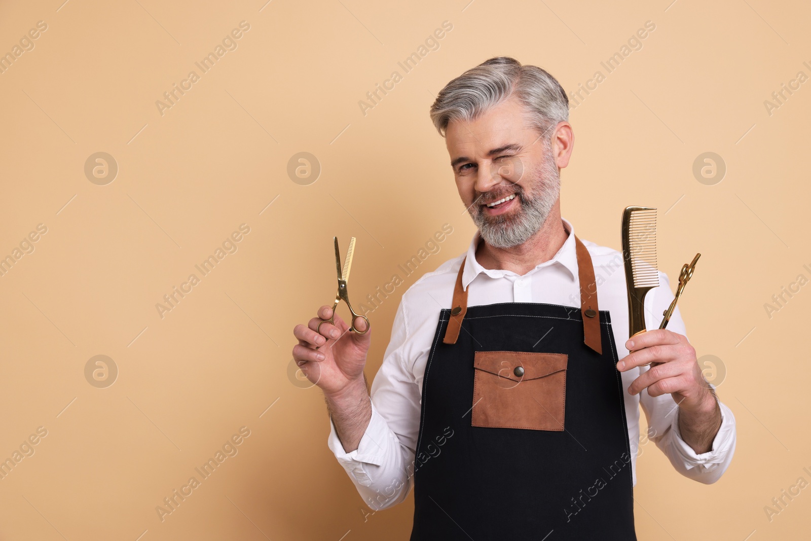 Photo of Smiling hairdresser with scissors and brush on beige background, space for text